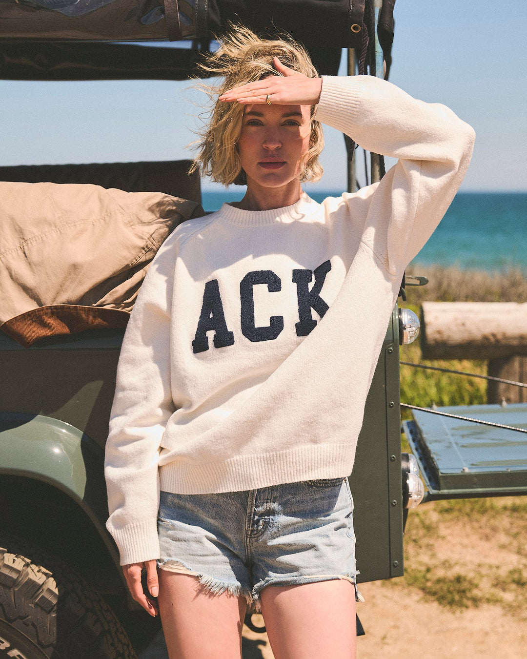 A woman wearing a cream-colored crewneck sweater with &