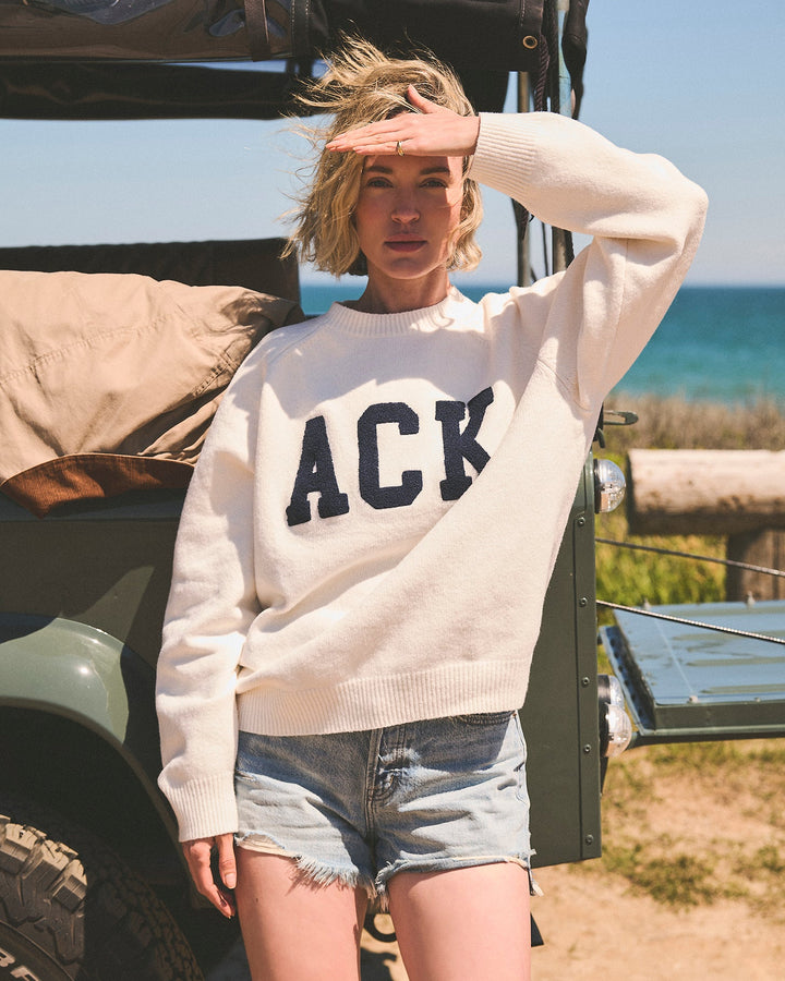 A woman wearing a cream-colored crewneck sweater with &