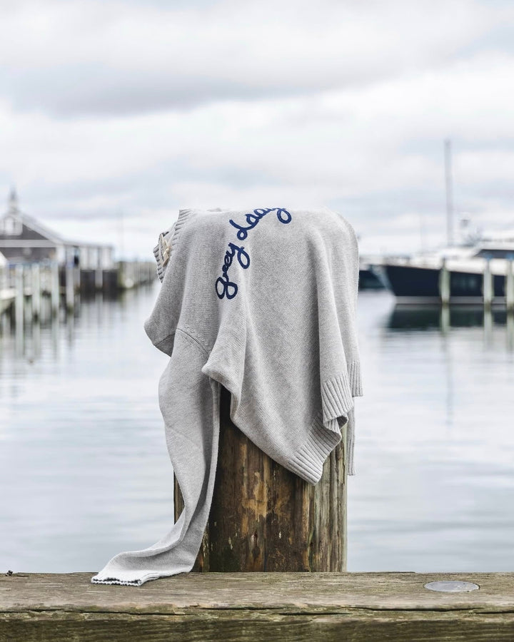 A light heather gray knit sweater with Grey Lady embroidered in navy blue script across the chest, draped over a wooden dock post. Classic Crew Sweater- Grey Lady by Ellsworth + Ivey.
