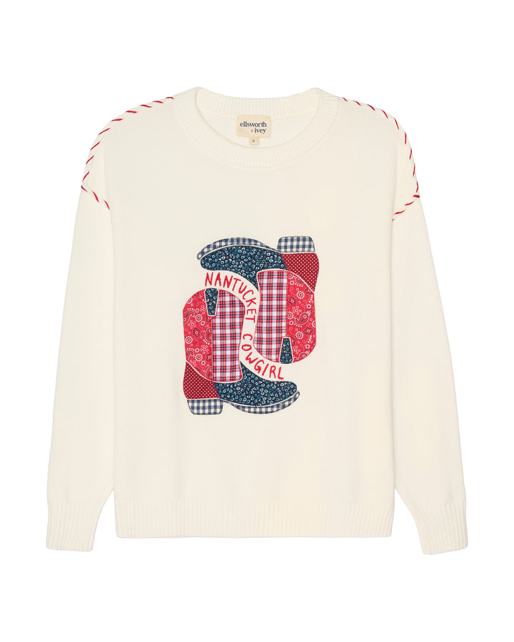 An off-white knit sweater with a colorful patchwork graphic on the chest featuring red and navy patterned boots and the words &