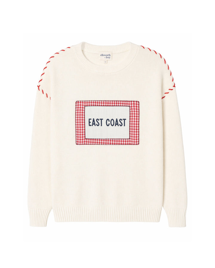 An off-white knit sweater with a red and white gingham graphic on the chest that reads &