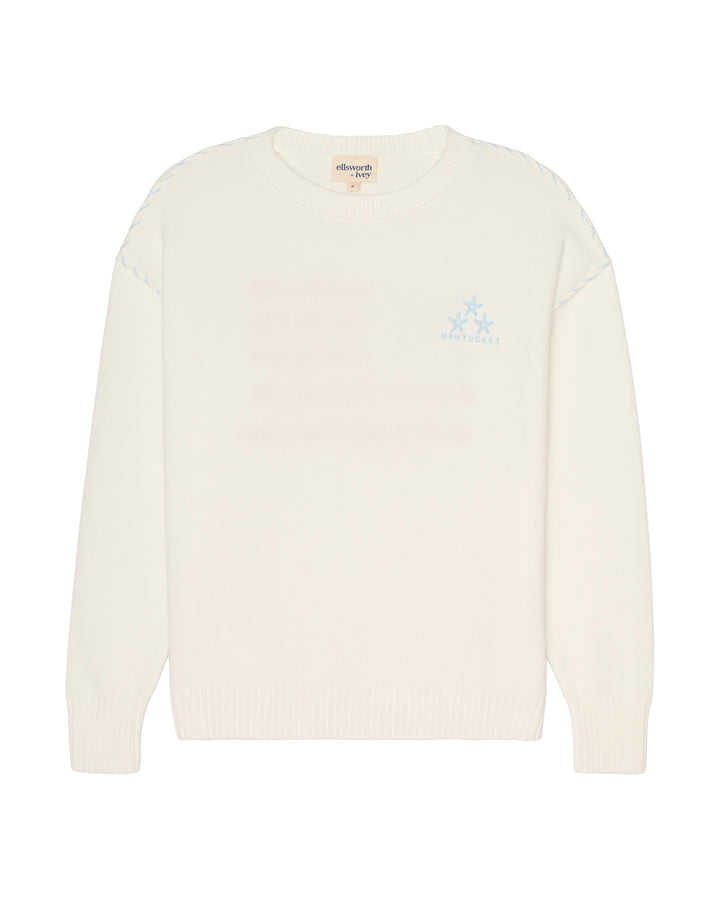 An off-white knit crewneck sweater with a light blue embroidered logo on the left chest, displayed against a solid white background. Ellsworth + Ivey Riley Stars and Shells Flag Sweater.
