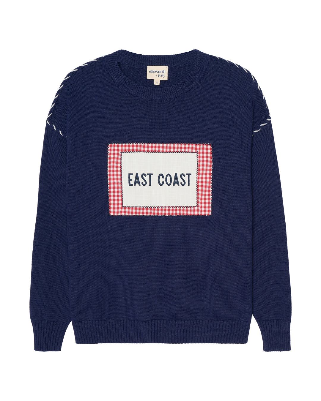 A navy blue crewneck women's sweater featuring a red and white gingham checkered square patch on the chest with the text 'EAST COAST' printed in blue. The sleeves have white dashed whip stitching on the drop shoulders. Ellsworth + Ivey Riley Crew - East Coast.