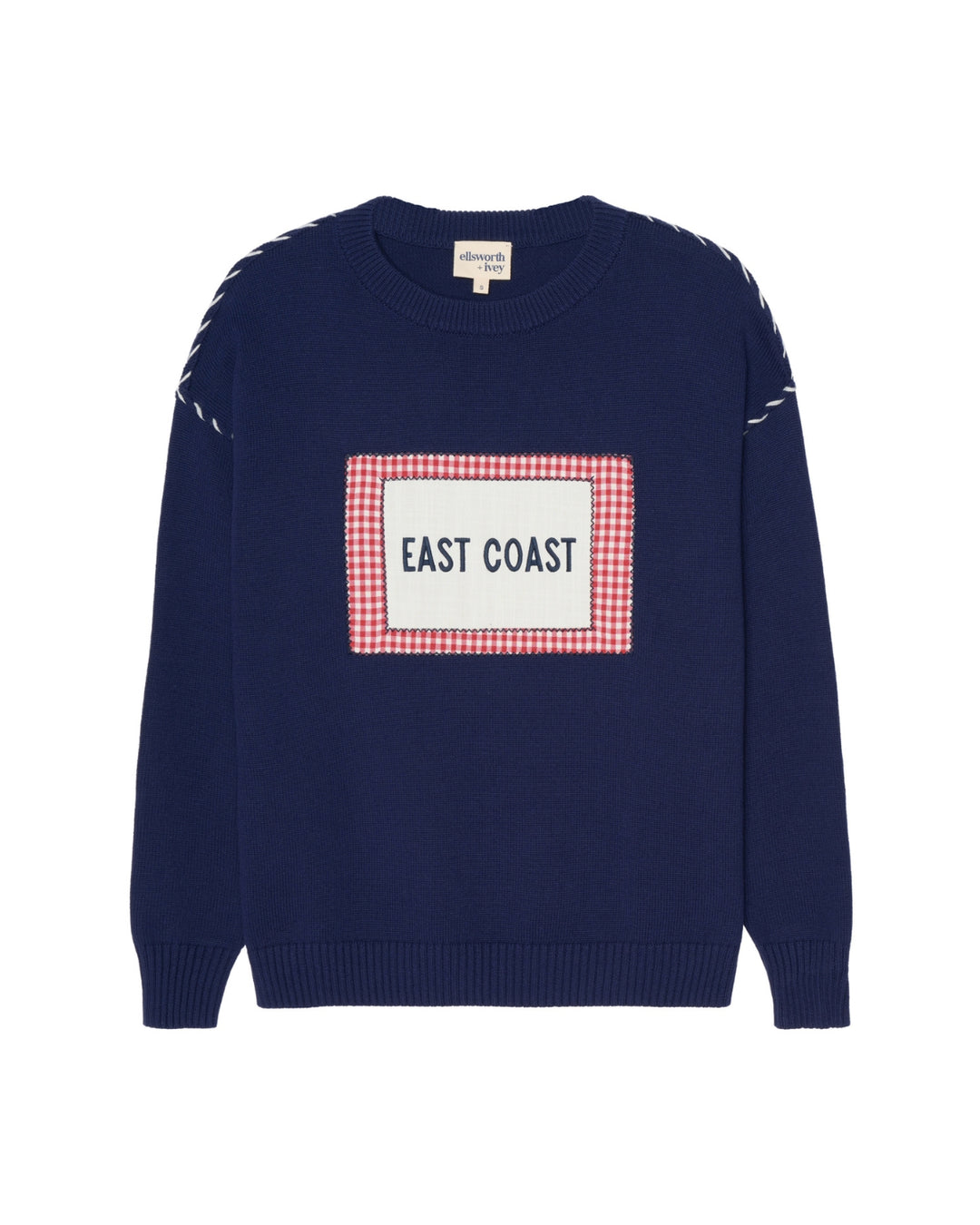 A navy blue crewneck women's sweater featuring a central rectangular patch with a red and white gingham border and the words 'EAST COAST' in navy. The sleeves have white whip stitch details near the shoulders. Ellsworth + Ivey Riley Crew - East Coast.