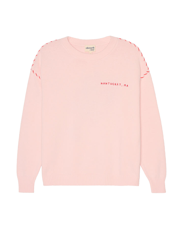 A light pink crewneck sweater with red dashed stitching along the shoulders and red text reading &
