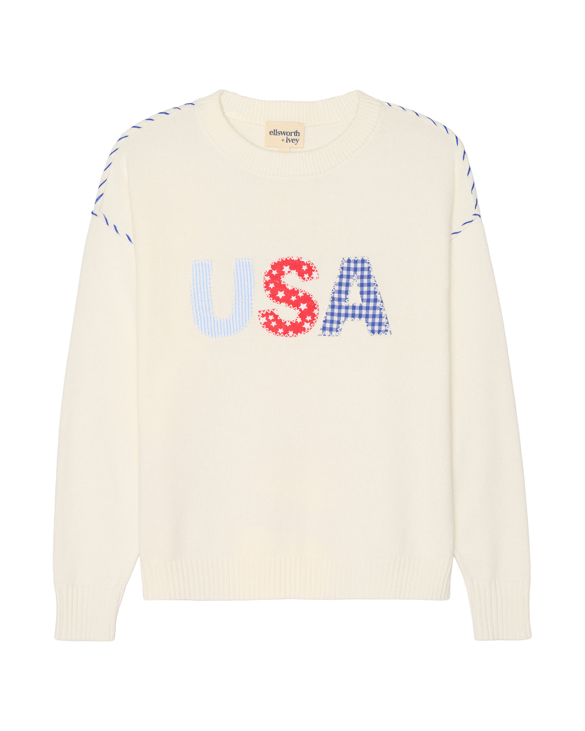An ivory off-white knit women's sweater featuring a large 'USA' patchwork graphic across the chest, with 'U' in light blue, 'S' in red with white dots, and 'A' in blue gingham. The sleeves have blue and white diagonal stripe details at the shoulders. Riley Crew - USA Patchwork by Ellsworth + Ivey.
