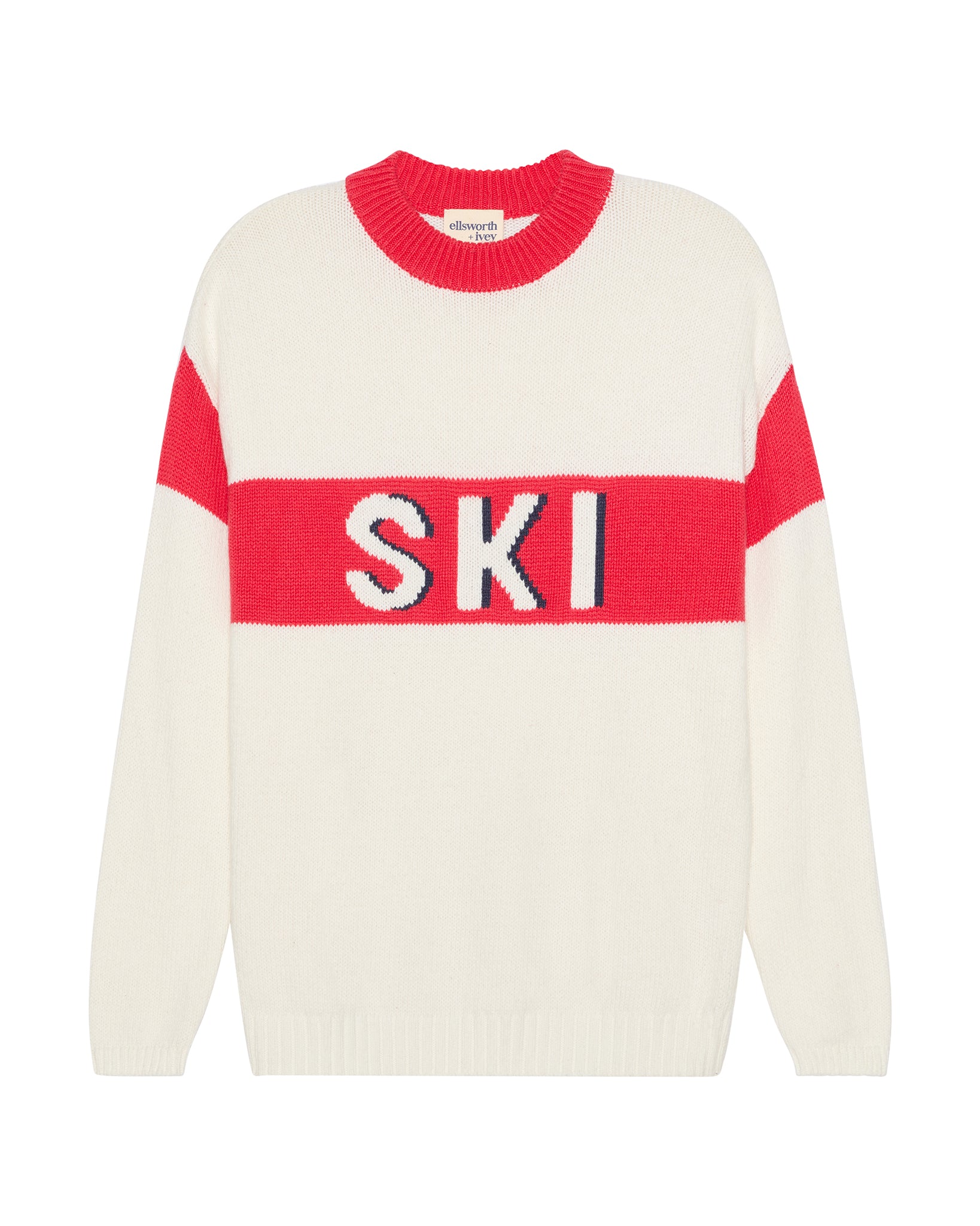 An ivory cream-colored knit women's sweater with a bold red horizontal chest stripe featuring the word 'SKI' in white letters outlined in blue. The sleeves and upper chest have red color-blocked sections, and the crew neck is also red. Sadie Crew - Ski in Ivory Red by Ellsworth + Ivey.