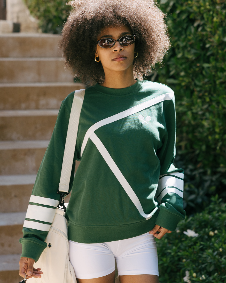 Woman wearing a green tennis sweatshirt with white accents and white shorts, standing outdoors. Elle Sweatshirt - Tennis Lines by Ellsworth + Ivey.