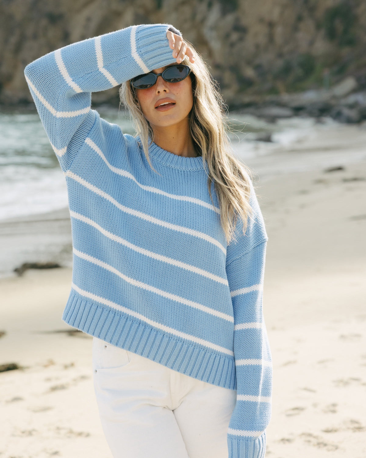 Woman wearing an oversized blue and white striped sweater on a beach. Elena Crew Sweater in Cornflower Blue/Ivory by Ellsworth + Ivey.