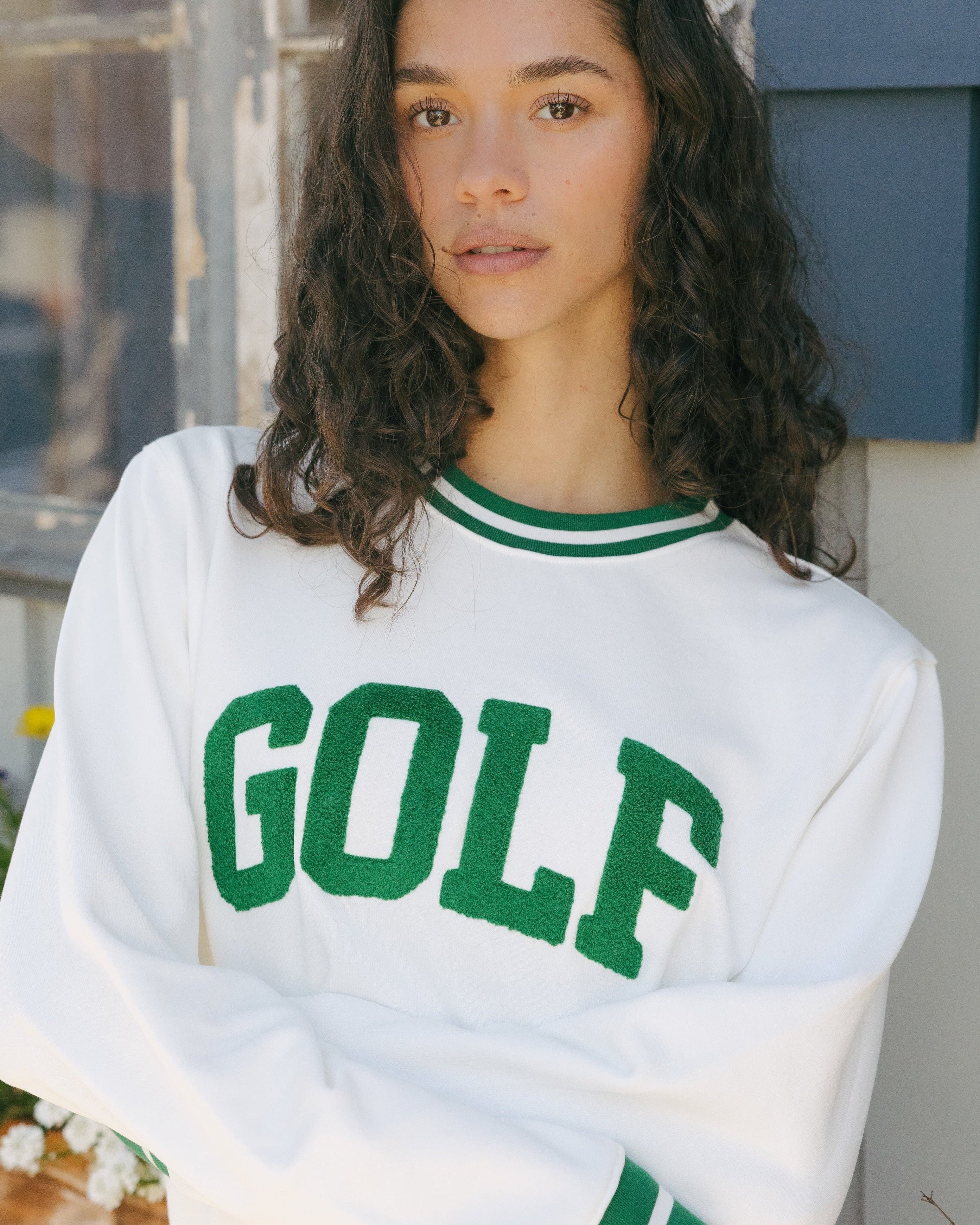 Woman wearing a white sweatshirt with 'GOLF' printed in green letters. Elle Sweatshirt - Collegiate Golf by Ellsworth + Ivey.
